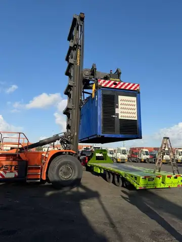 A containerized generator lifted by a reach stacker onto a trailer.