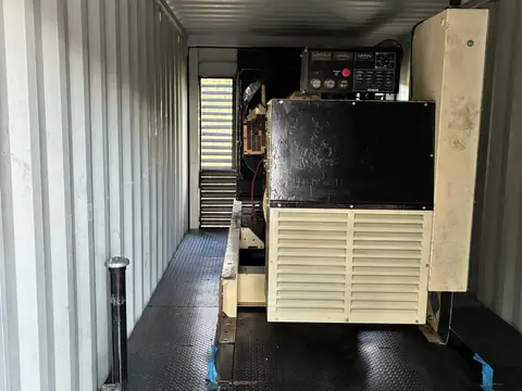 Cream-coloured Kohler generator enclosure inside a container, control panel on top.